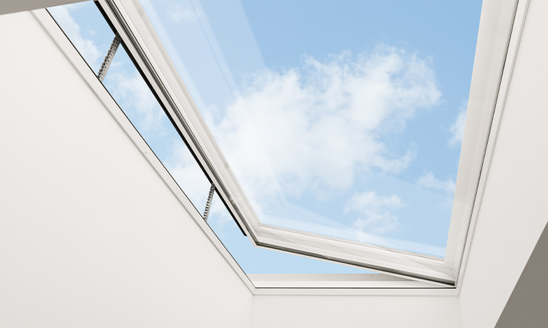 Åpen takluke med hvit ramme mot klar blå himmel med lette skyer