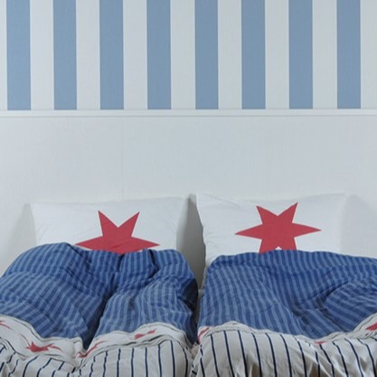 To senger med blåstripete dyner og hvite puter med røde stjerner foran stripet vegg