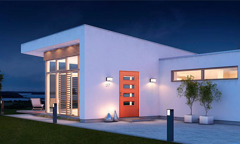 Moderne hvitt funkishus ved sjøen om kvelden, rød inngangsdør med glassruter og utelys