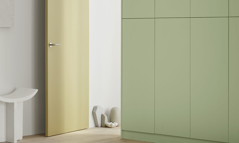 Minimalistisk interiør med gult dørblad, lysegrønne skap og hvite dekorformer på lyst tregulv.