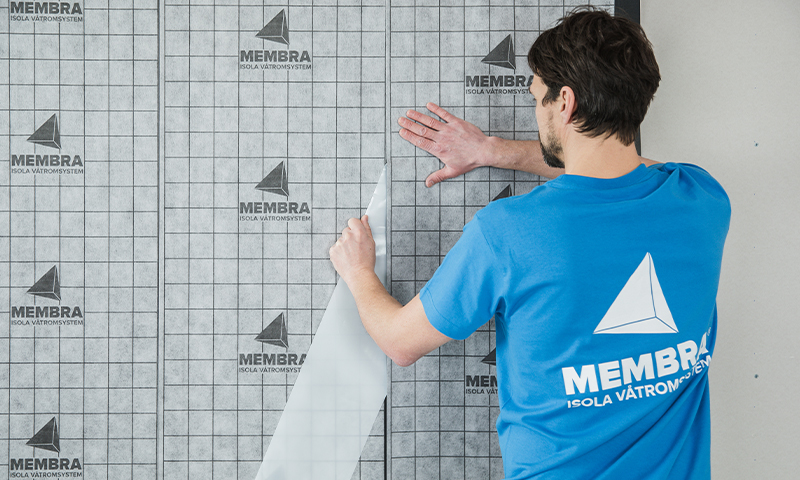 Håndverker i blå Membra-t-skjorte fester grå vanntett membran med rutemønster og logo.