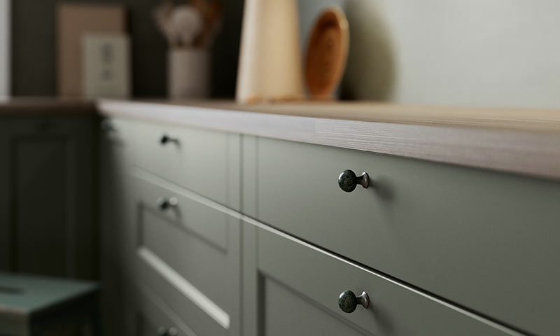 Nærbilde av lysegrønne kjøkkenskuffer med mørke grønne knotter og lys treplate.