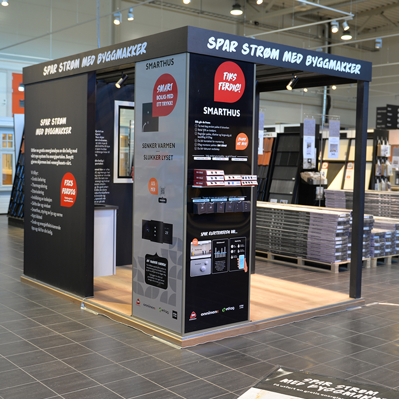 Svart smarthus-stand i Byggmakker-butikk med hvit «Spar strøm»-tekst og røde infoknapper