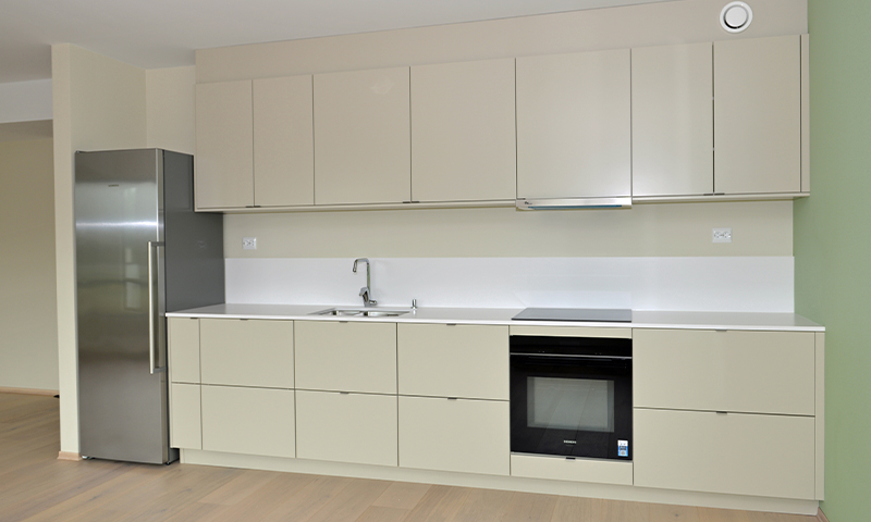 Moderne lys kjøkkeninnredning med beige skap, stålfrigo, innebygd ovn og vask