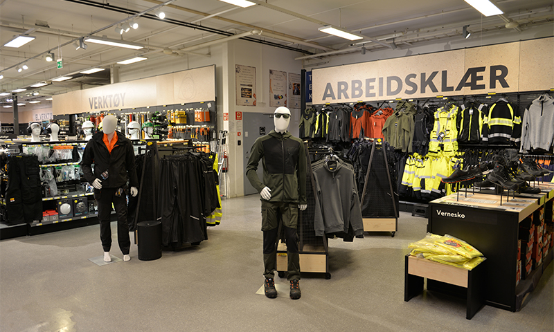 Butikkinteriør med arbeidsklær: to mørke mannekenger, hyller med gule refleksjakker og vernesko