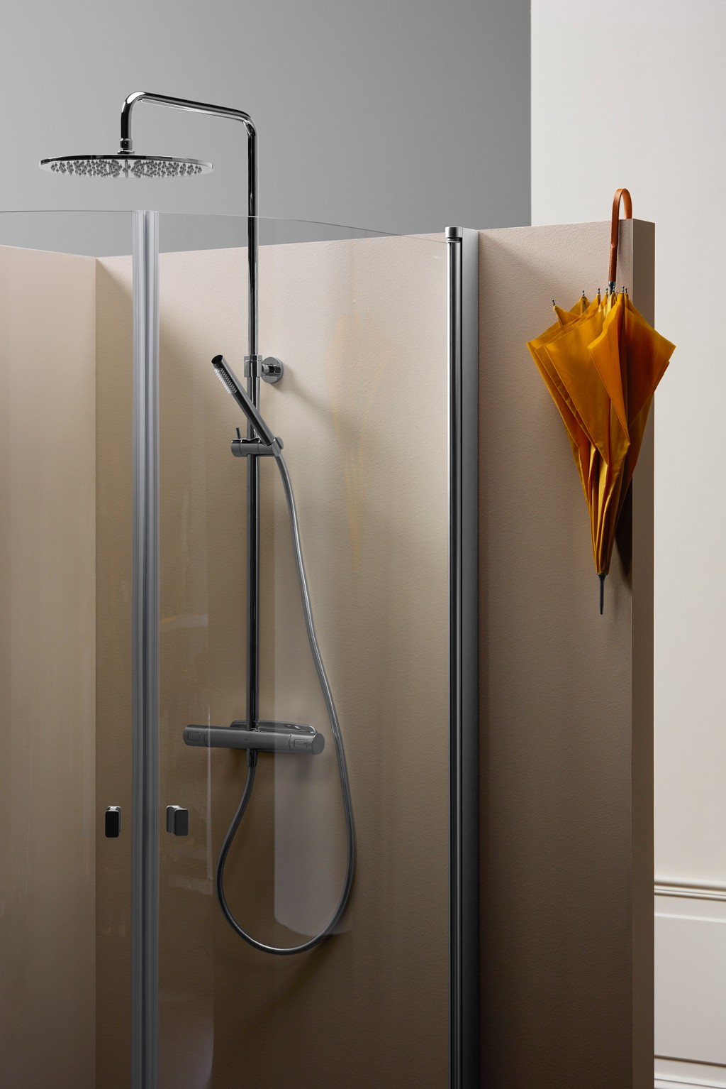 Moderne dusjkrok med glassdør, krom regn- og hånddusj mot beige vegg, gul paraply hengende.