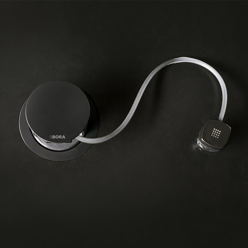 Sort rund BORA-kontroller med sølvfarget flettet slange til svart firkantet enhet