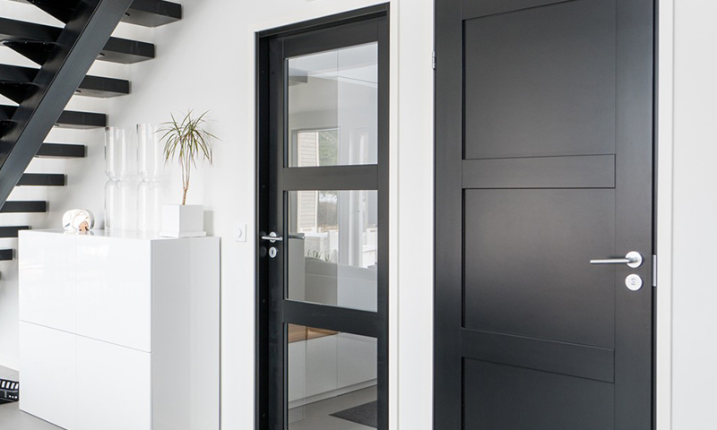 Hvit gang med sort trapp, hvitt skap med vaser, to svarte dører – én med glassfelt