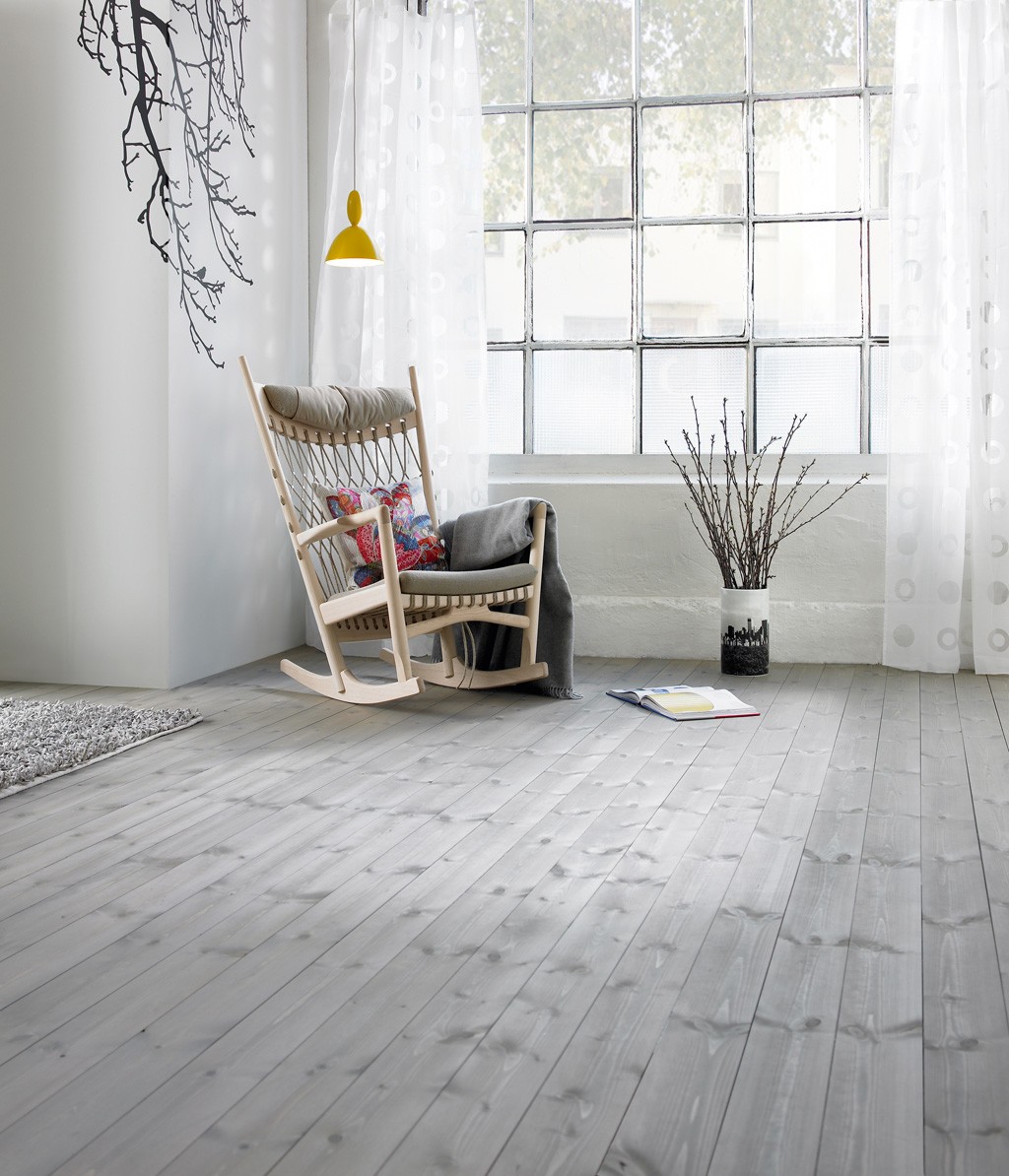 Lyst rom med gyngestol i lyst tre, fargerik pute, gul lampe, stort vindu og kvister i vase