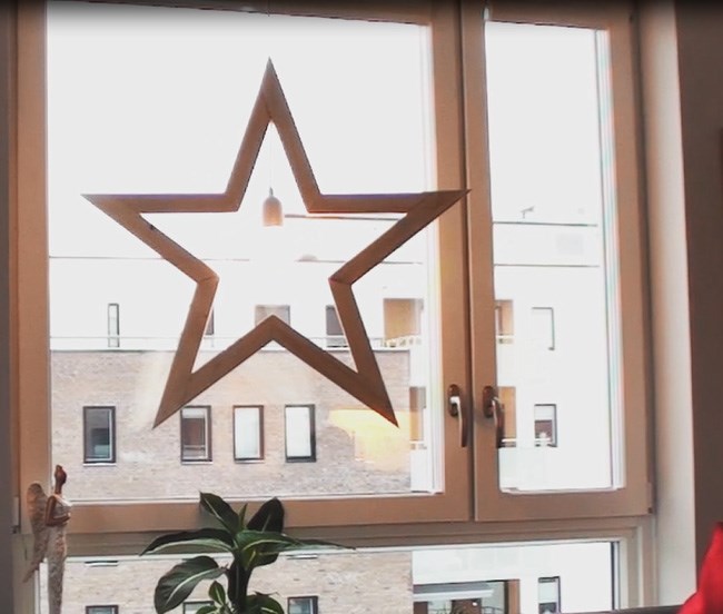 Lys trestjerne hengende i vindu med utsikt til mursteinsbygning og grønn potteplante.