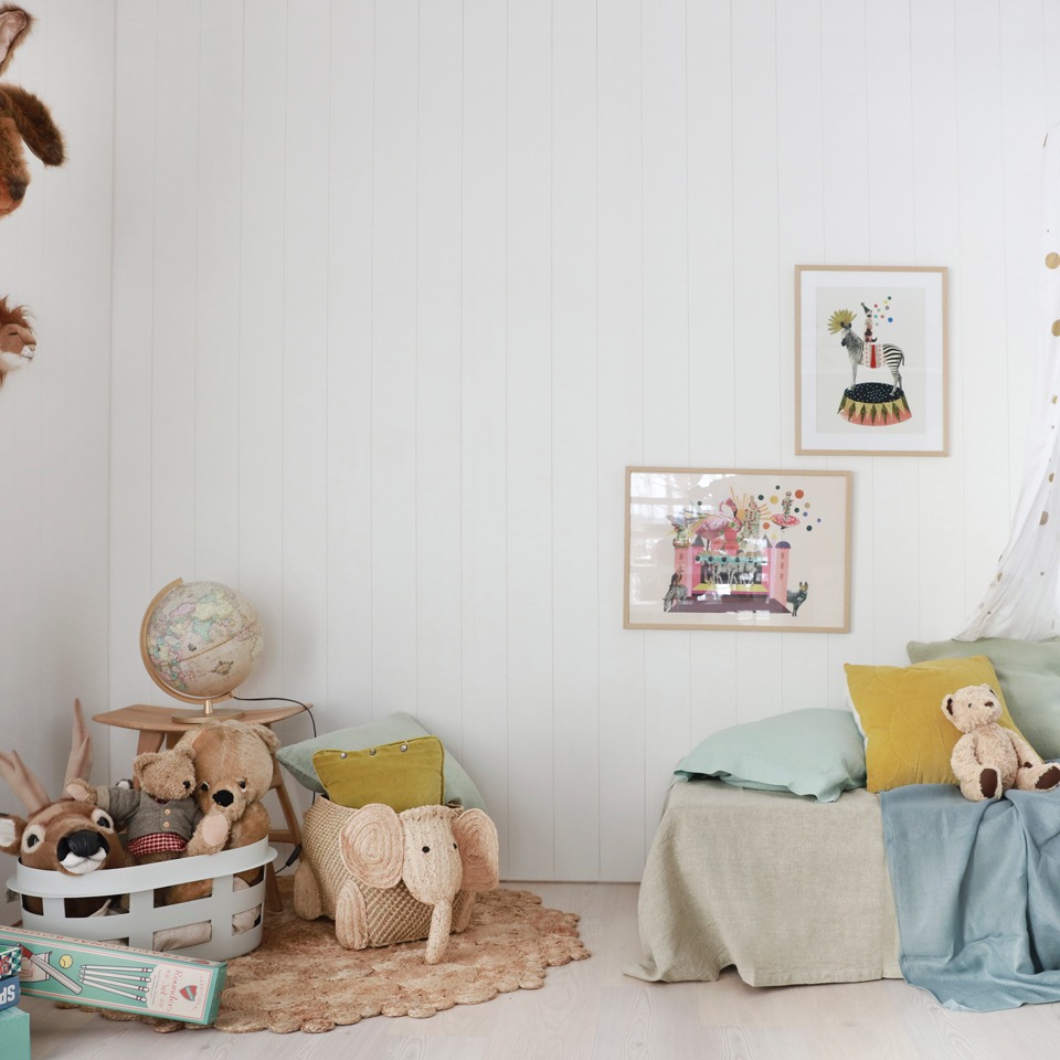 Barnerom med hvite panelvegger, pastellputer, bamser, elefantkurv, globus og plakater