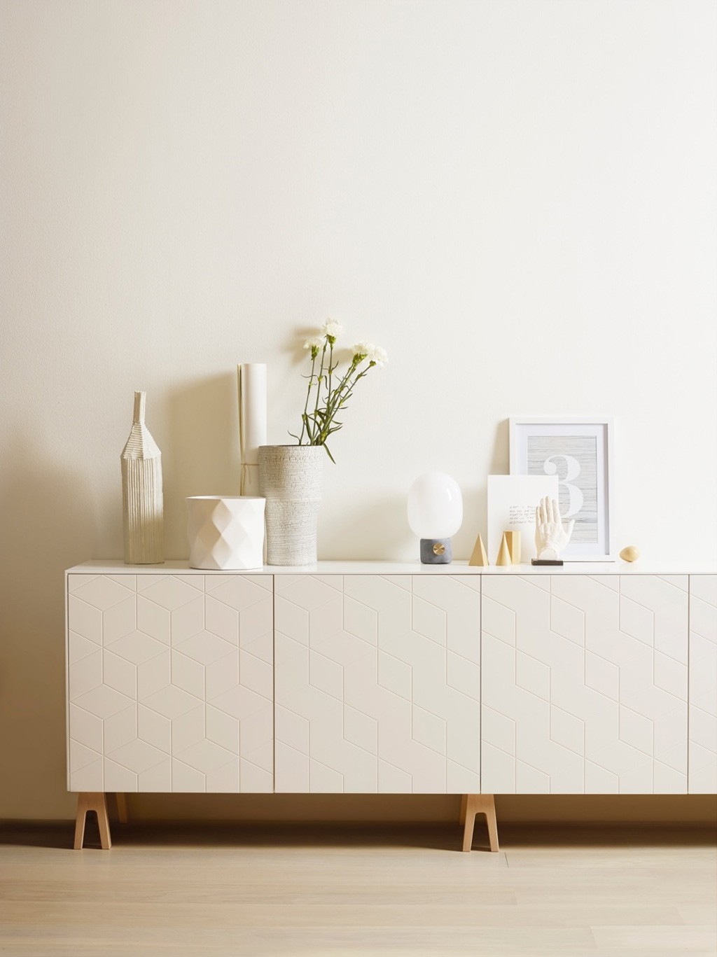 Hvitt geometrisk skjenk med vaser, hvite blomster, bordlampe, ramme med 3 og gullobjekter