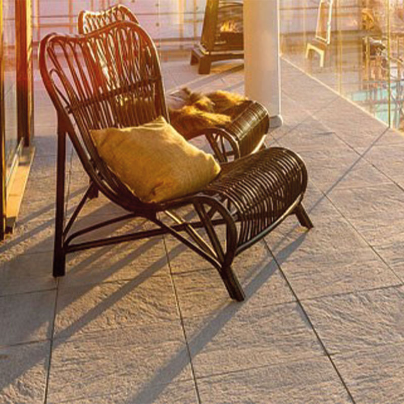 To mørke rottingstoler med gul pute og skinnteppe på solbelyst flislagt balkong med glassrekkverk