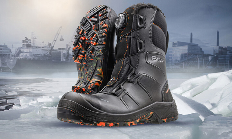 Paret svarte Sievi-vinterstøvler med oransje detaljer og kraftige gummisåler på is