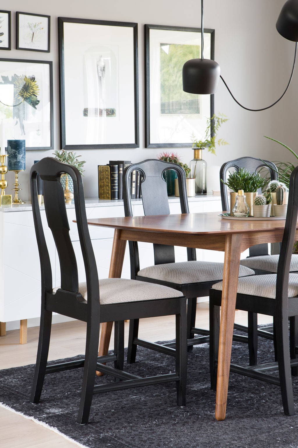 Moderne spisestue med trebord, svarte stoler, sort teppe, hvit skjenk med grønne planter