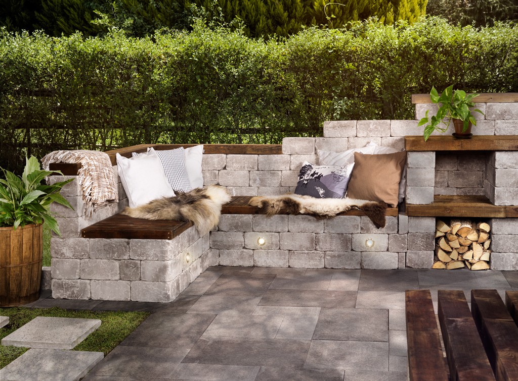 Hjørnesofa ute av grå betongblokker med treflate, pels, hvite og brune puter og grønne planter