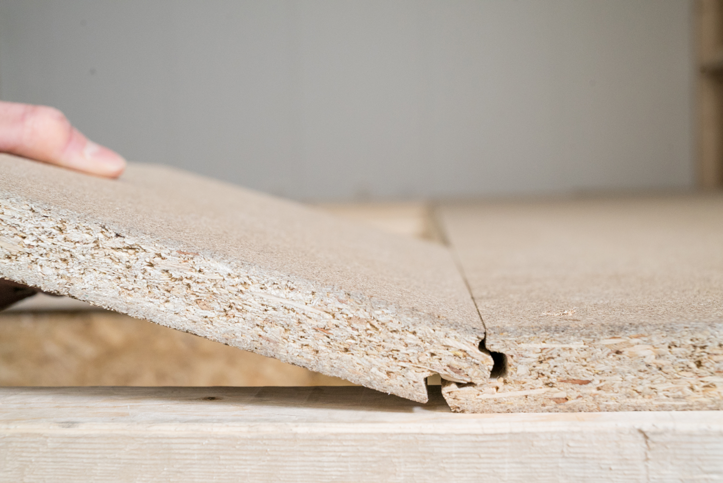 Hånd løfter beige sponplate med not- og fjærfeste under legging.