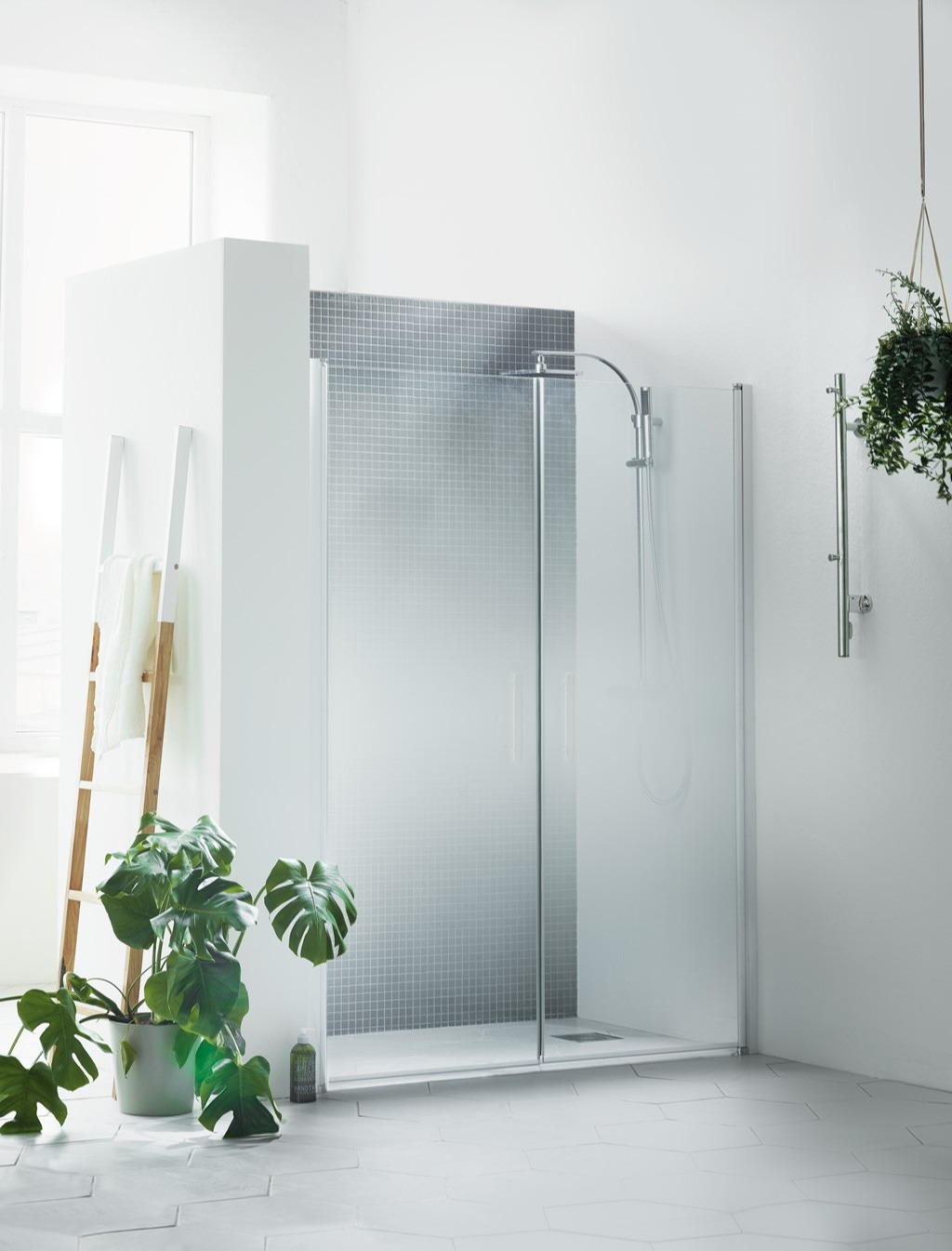 Lyst baderom med glassdusj, grå mosaikkfliser, trestige med håndkle, gulv- og hengeplanter.