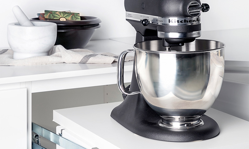 Svart KitchenAid-kjøkkenmaskin med rustfri stålbolle på hvit benkeplate ved morter.