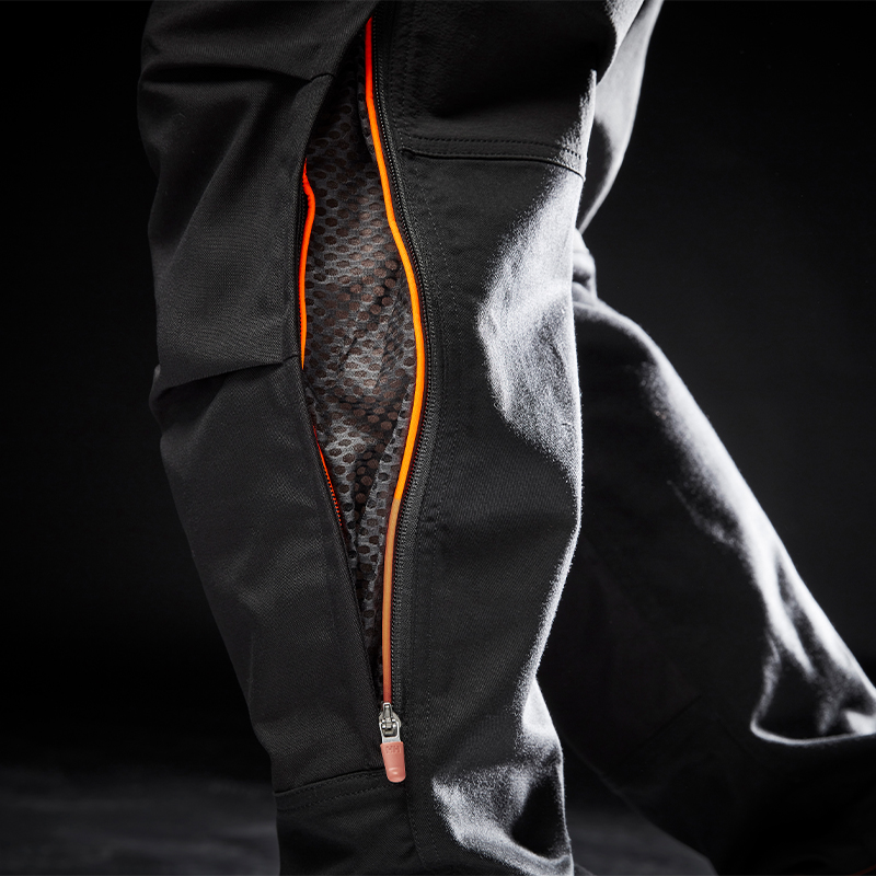 Nærbilde av svart teknisk bukse med åpen oransje glidelås som viser grått bikakemønster.