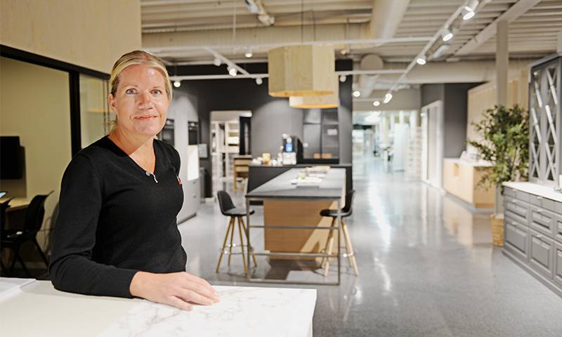 Person i svart genser ved hvit marmorbenk i kjøkkenutstilling med mørke grå skap og tremøbler