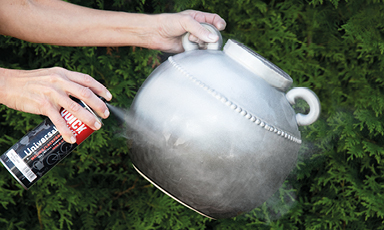 Hender sprayer lakk på en metallurne foran grønn hekk.