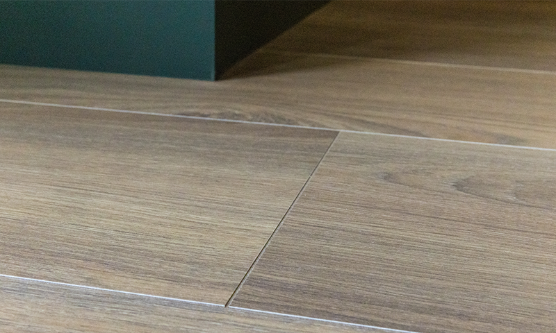 Lyst brunt tregulv med synlige skjøter mot en mørkegrønn sokkel