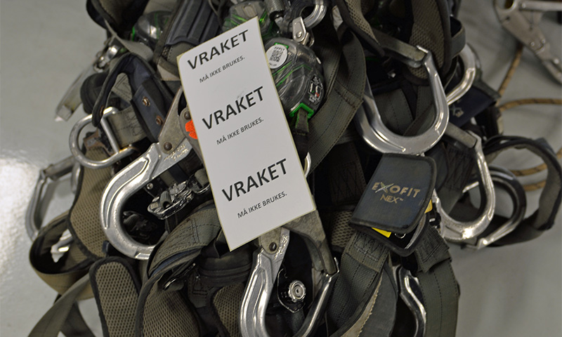 Grå fallsikringsseler med blanke metallkroker og hvite "VRAKET"-merkelapper.