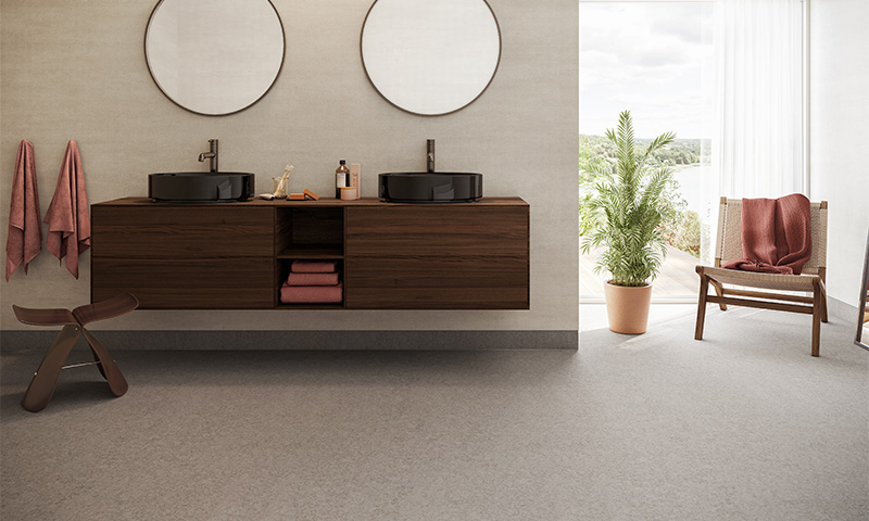 Lyst baderom med mørkt tre-svevende skap, sorte vasker, speil, rosa tekstiler, grønn potteplante.