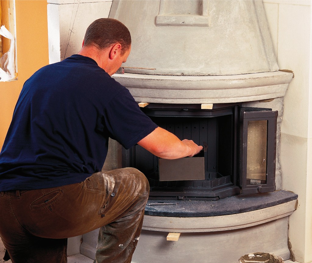 Mann i blå skjorte installerer svart peisinnsats i lys grå murpeis