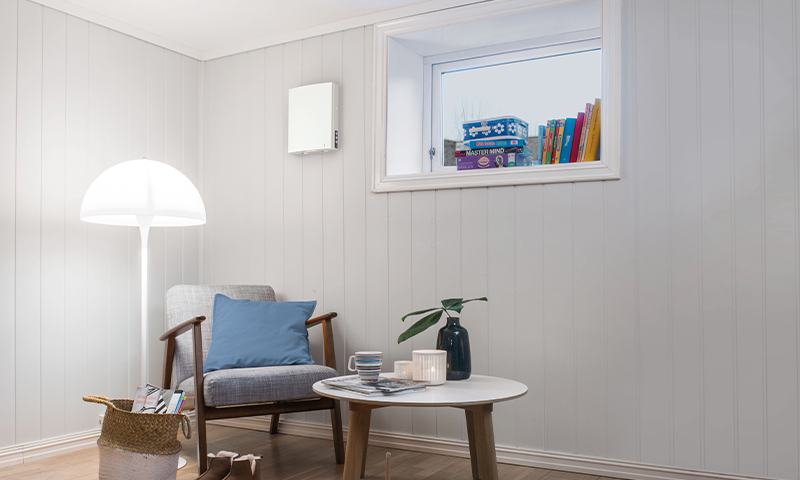 Lyst lesehjørne med grå lenestol, blå pute, hvit gulvlampe, rundt bord med grønn vase, spill i vindu