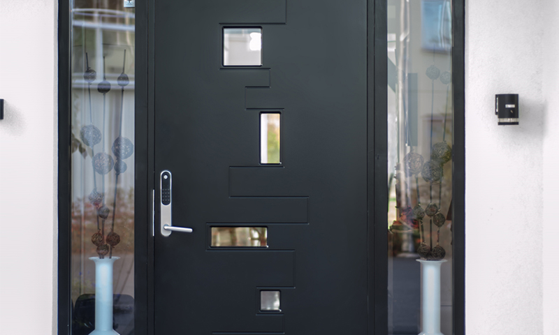 Moderne svart inngangsdør med små vinduer, sølvhåndtak og tastatur, glassfelt med vase, hvit fasade