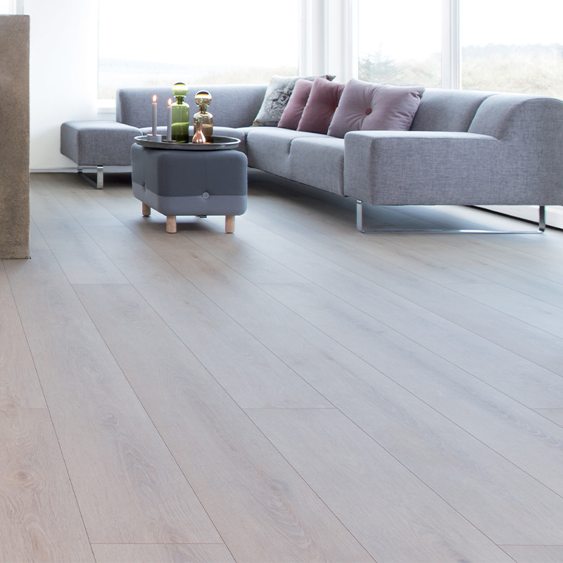 Lyst stueinteriør med grå sofa, rosa puter, puff med glasspynt og lyst tregulv