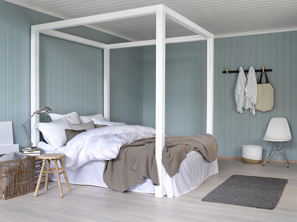 Lyst soverom med hvit himmelseng foran duse blå vegger, grått pledd, kurv og stol