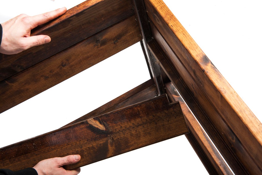 To hender skyver mørkebrun treplanke inn i treramme mot hvit bakgrunn