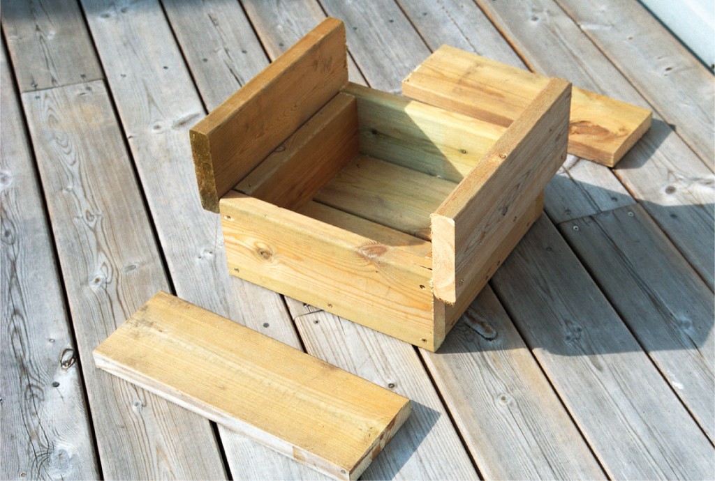 Uferdig lys trekasse med løse planker på grå terrassebord i sollys