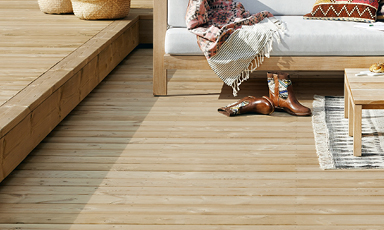 Lyse treplanker som gulv, hvit sofa med rosa mønstret pledd og brune cowboystøvler.