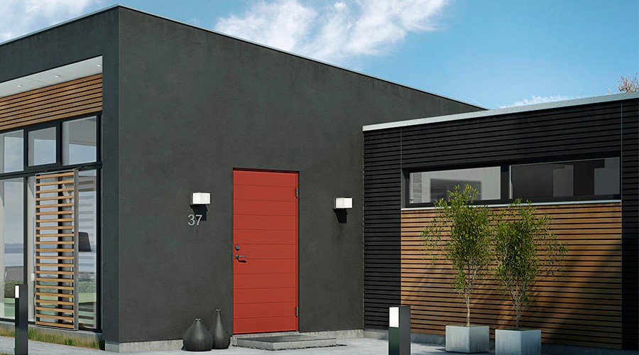 Moderne svart hus med rødt inngangsdør, store glassvinduer og trekledning under blå himmel.