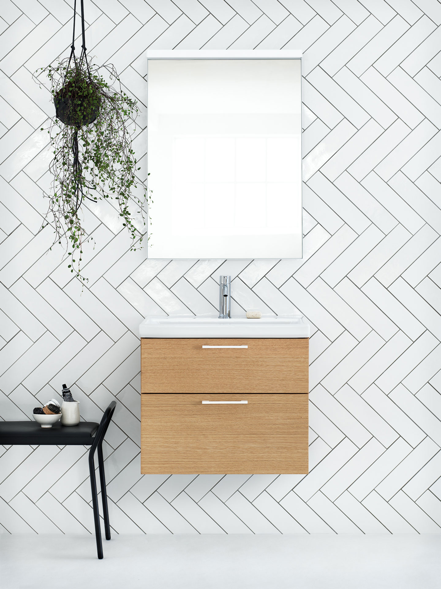 Moderne baderom: hvit fiskebeintflis, hengende plante, eikevask med speil, svart benk.