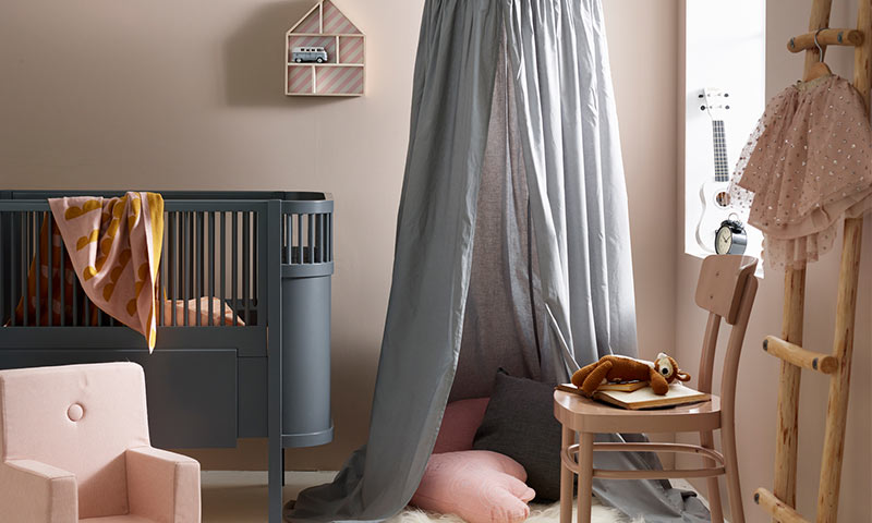 Barnerom med mørkegrå sprinkelseng, rosa lenestol, grå himmelseng, trestol med kosebamse.