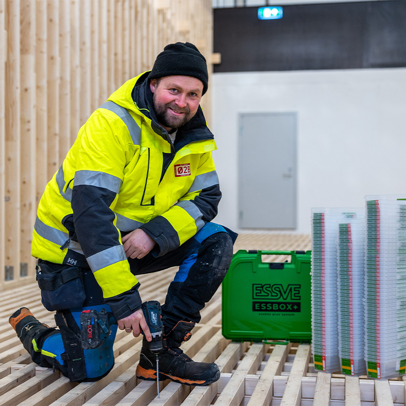 Gulkledd bygningsarbeider skrur trelekter mens grønn ESSVE-verktøykasse står ved siden.