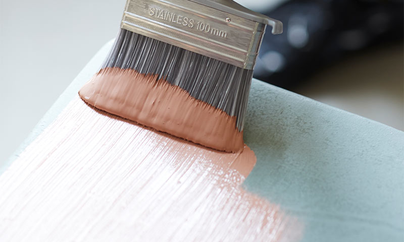 Pensel med rustfri 100 mm ferrule maler ferskenrosa strøk over mintgrønn flate.