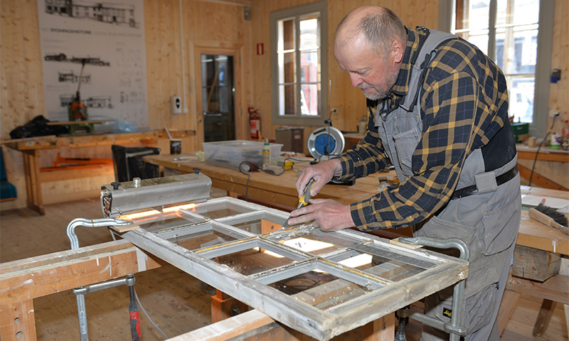 Tømrer i rutet skjorte skraper vindusramme med meisel i lyst treverksted