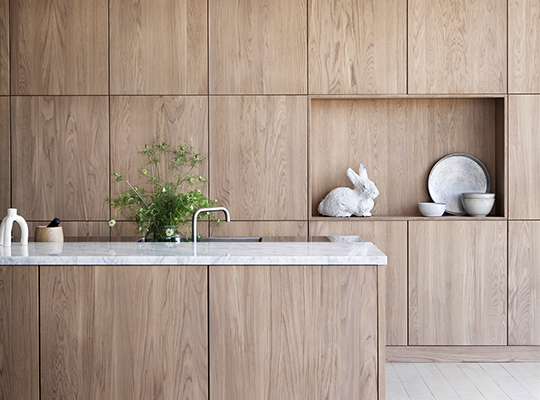 Moderne kjøkken med lyse tremøbler, marmorbenkeplate, grønn plante og hvit kaninskulptur.