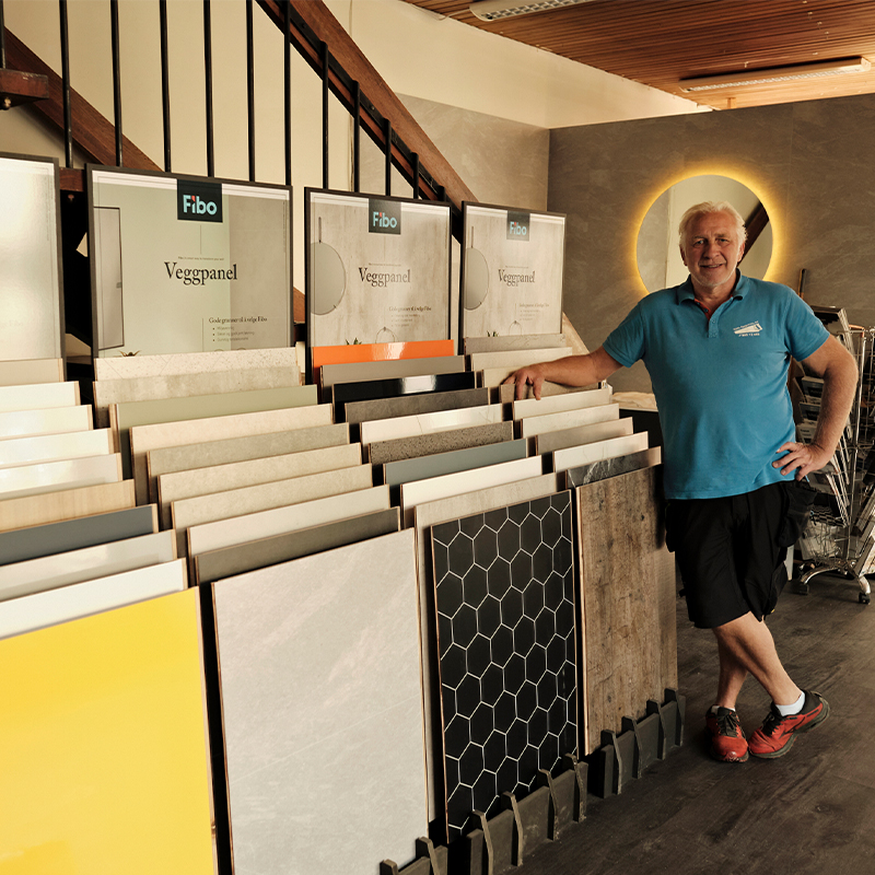 Mann ved stativ med Fibo veggpanelprøver i gult, hvitt, svart sekskantmønster og trestruktur.