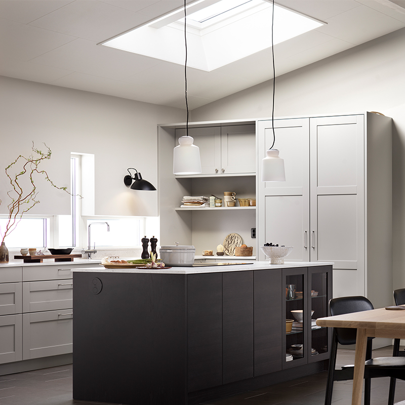 Lyst, minimalistisk kjøkken med svart kjøkkenøy, hvite skap, takvindu og hengelamper