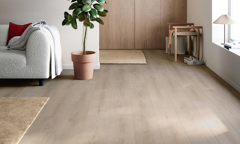 Lyst stuehjørne med lyst tregulv, hvit sofa med rød pute, potteplante og trebenk