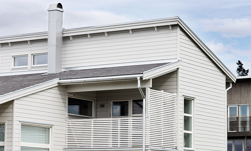 Moderne hvitt trehus med skråtak, pipe og hvit spileveranda.