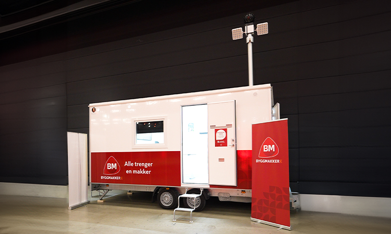 Rød-hvitt Byggmakker-vogn i messehall med logo og teksten «Alle trenger en makker»