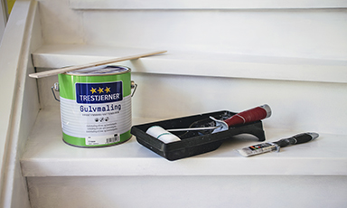 Kanne med gulvmaling, malerulle og pensel på hvite trapper.